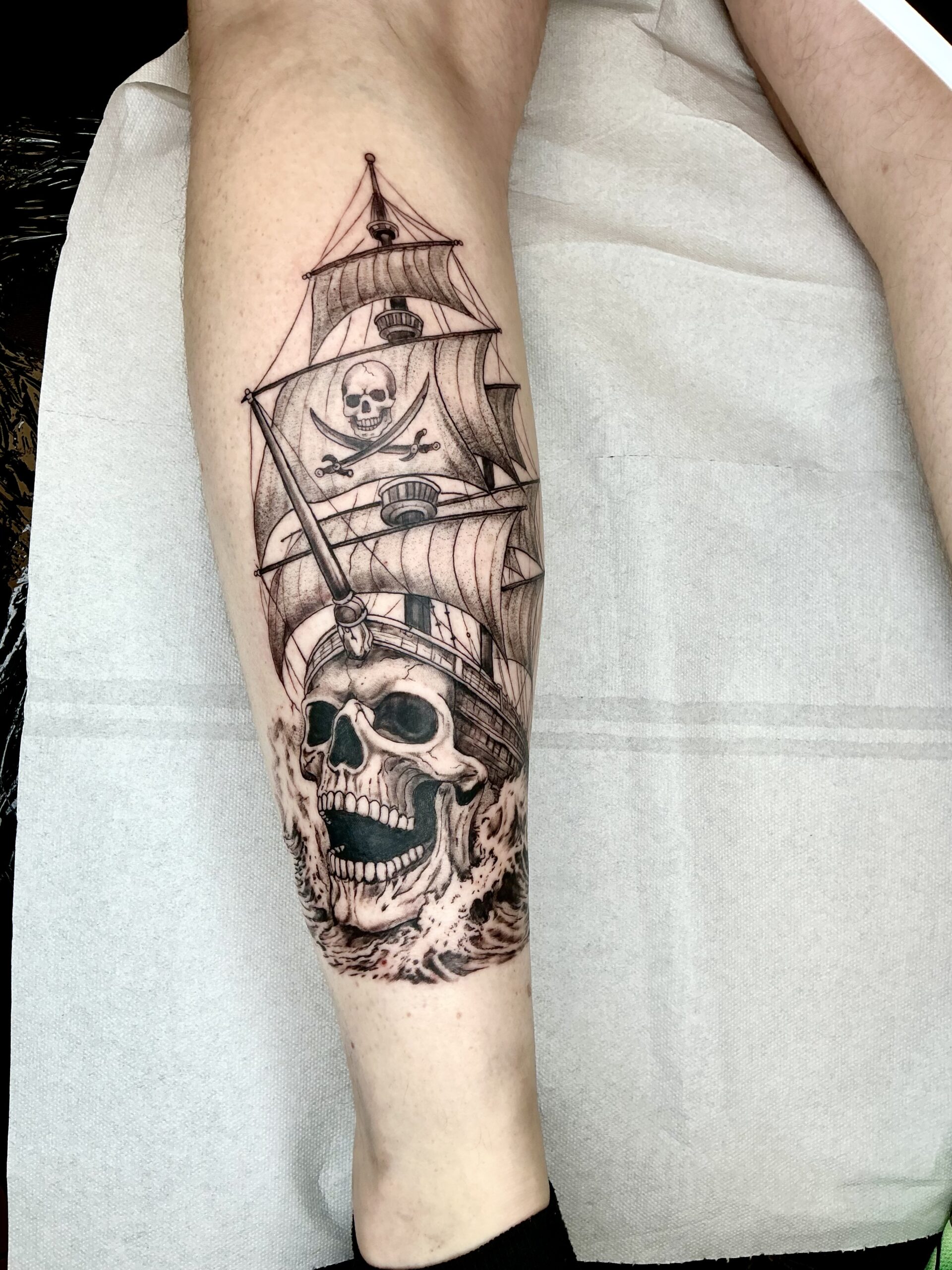 Tatouage bateau pirate et crâne en cours sur le mollet